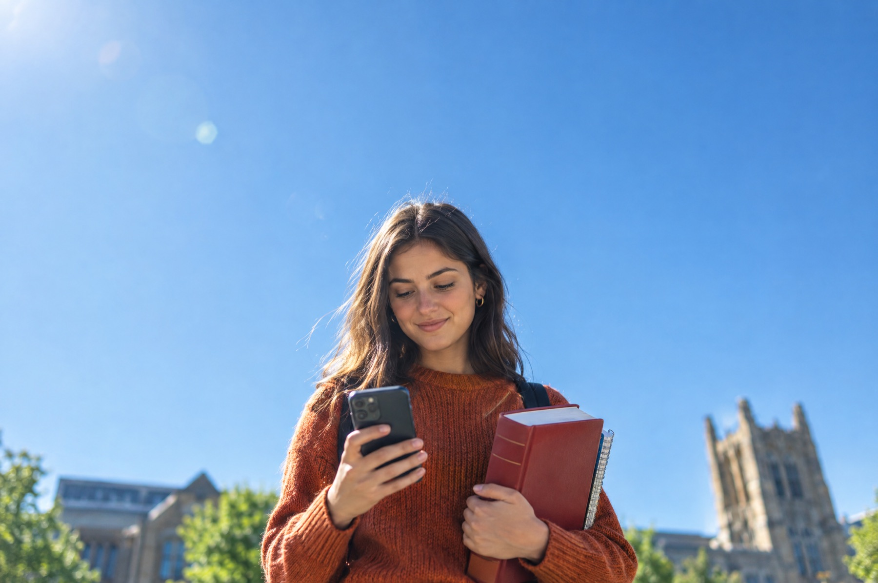 Jurastudentin mit Smartphone und roten Gesetzbüchern vor blauem Himmel